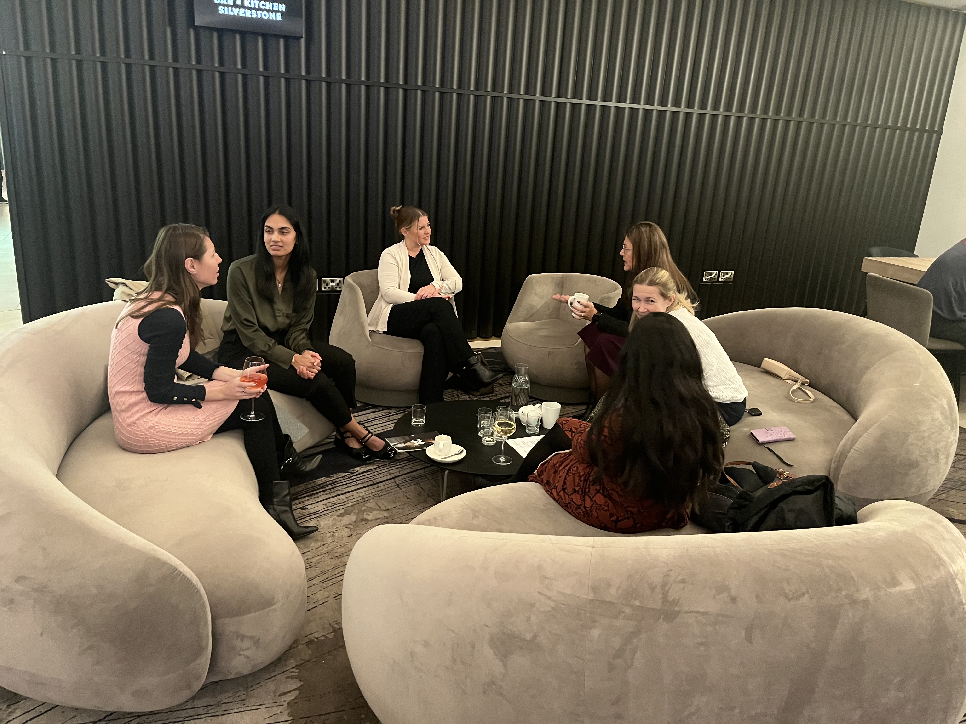 A group of women networking over drinks at Bar and Kitchen Silverstone, seated in curved lounge chairs around a low table.